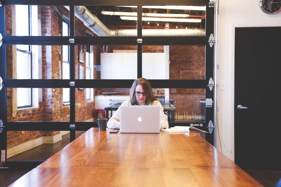 A young woman works on a laptop in a modern office with exposed brick walls.
