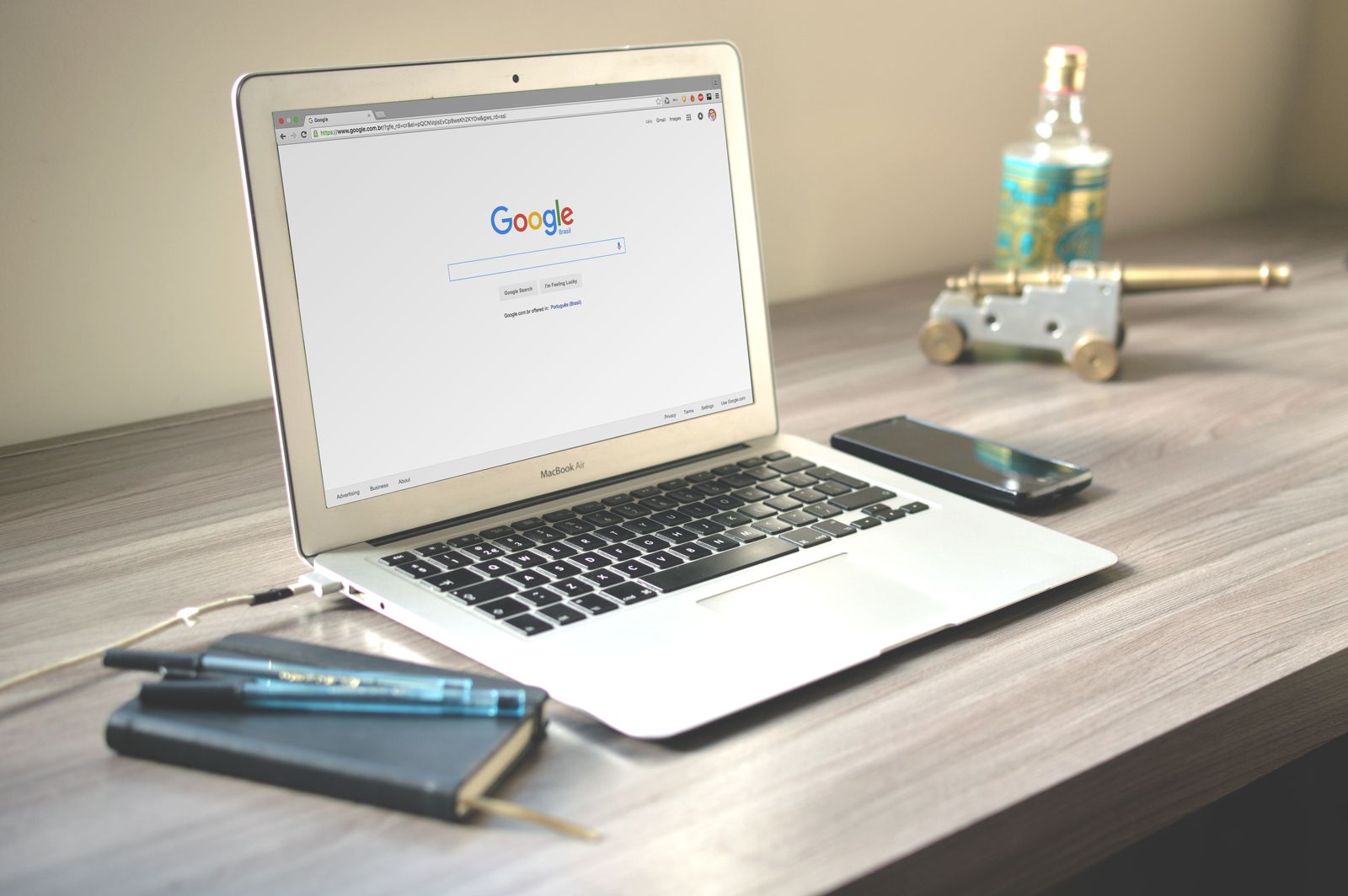 Laptop on a wooden desk showing the Google search page, next to a smartphone and notebook