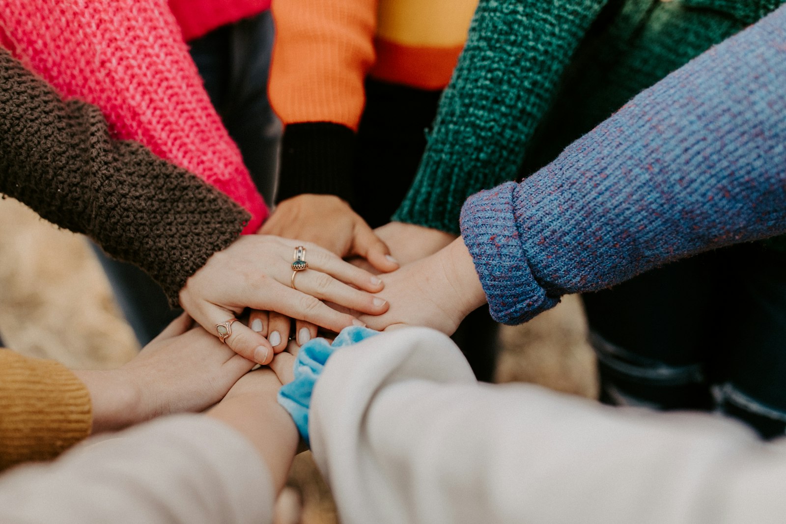Group of volunteers in colorful sweaters stacking their hands together