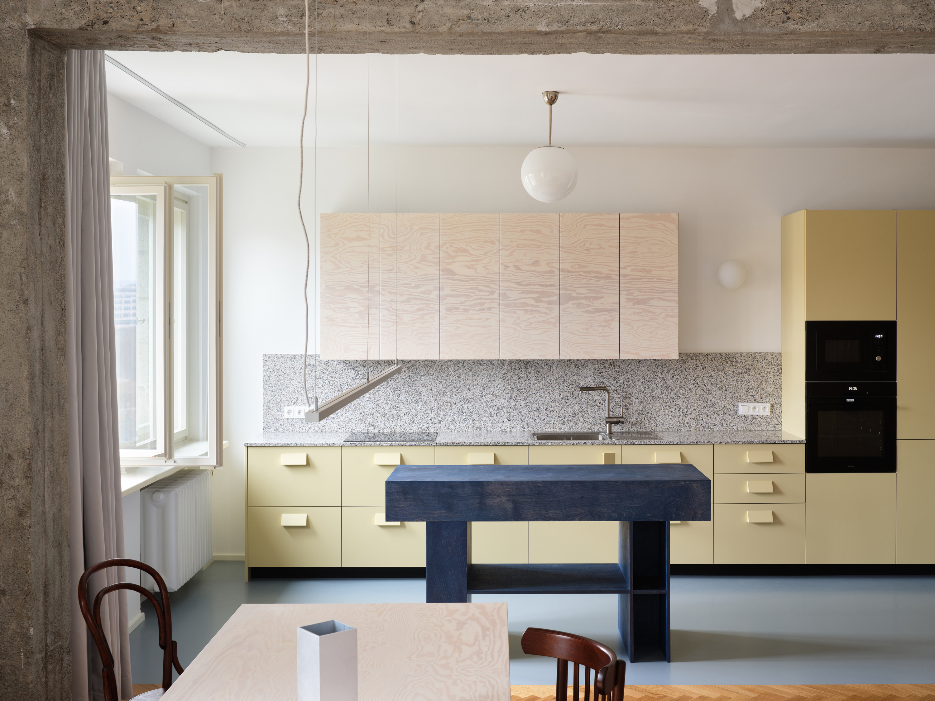 A renovated Prague apartment interior combining raw concrete surfaces with soft pastel-coloured furnishings and walls.