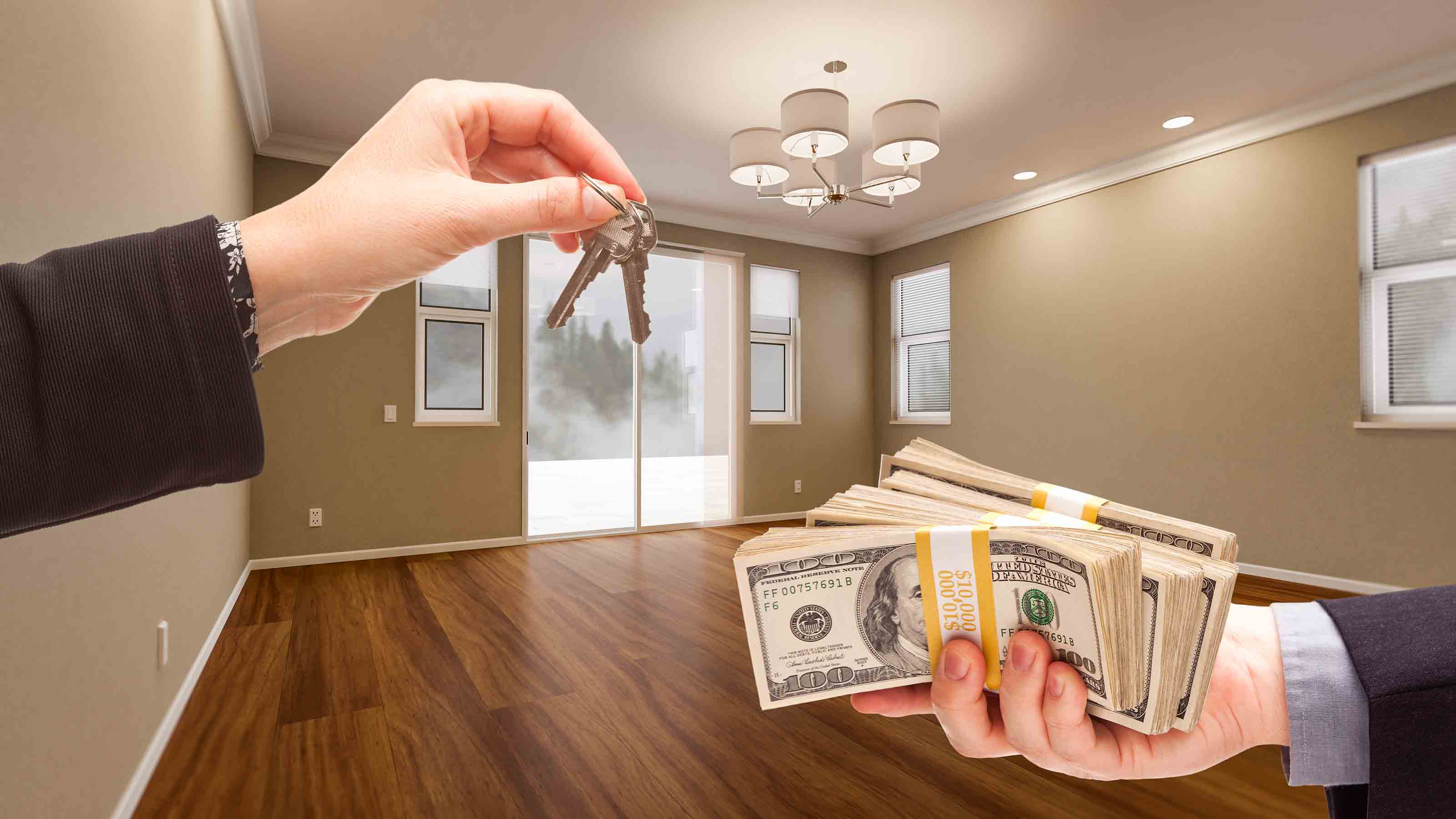 A stack of US hundred-dollar bills, fanned out, with a house key resting on top.