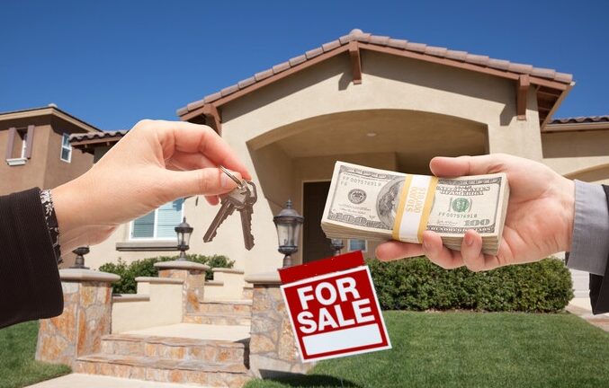 A person stands in front of a house, holding a 'Sold' sign with a key dangling from it, indicating a recent home sale.