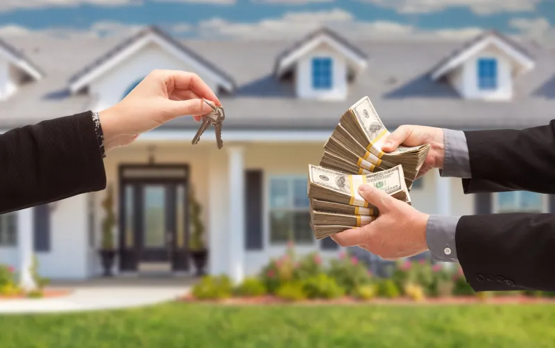 A person hands a stack of cash to another person, symbolizing a cash transaction for a house.